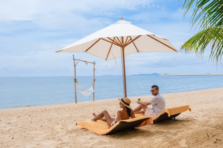 Men and women on the beach are relaxing in a beach chair on a sunny day with a hammock in Pattaya Thailand Ban Amphur beach. couple walking on a tropical beach with palm trees and hammock