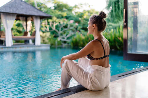 Woman relaxing by a luxury private villa pool surrounded by tropical gardens, enjoying a serene wellness retreat experience in Mexico.