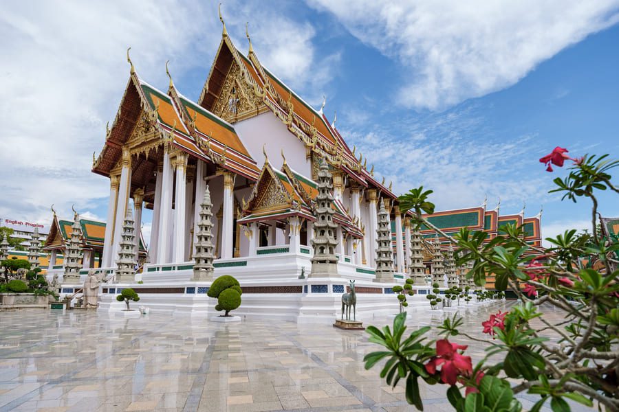 Ornate golden temple architecture at Wat Suthat Thepwararam in Bangkok, Thailand, captured under bright blue skies.