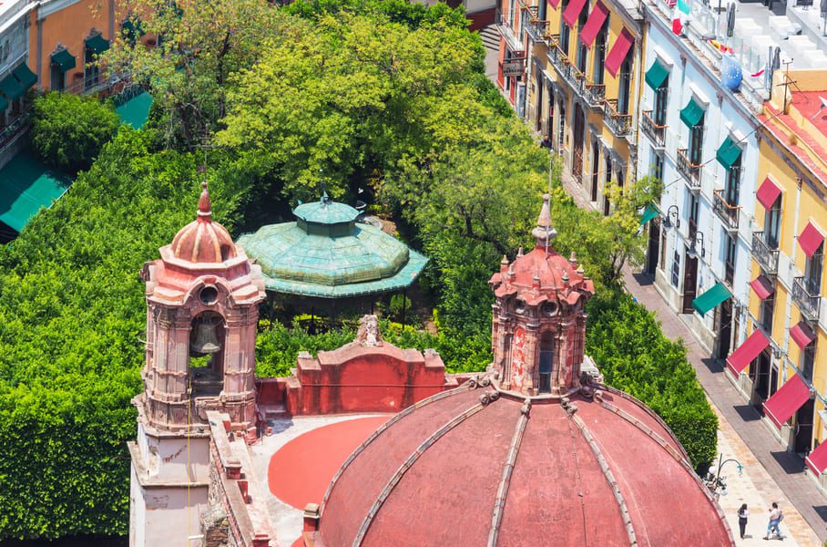 Aerial view of colourful colonial buildings, a domed church, and tree-lined plaza in Querétaro, Mexico.