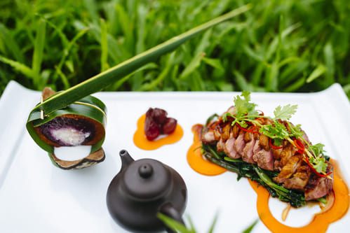 Gourmet Thai fine dining dish featuring seared duck breast with coconut dessert, served in a luxury garden restaurant setting.