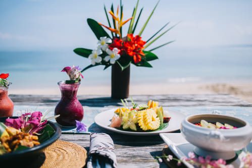 Elegant beachfront dining setup with tropical flowers, fresh gourmet dishes, and ocean views at a luxury resort in Mexico.