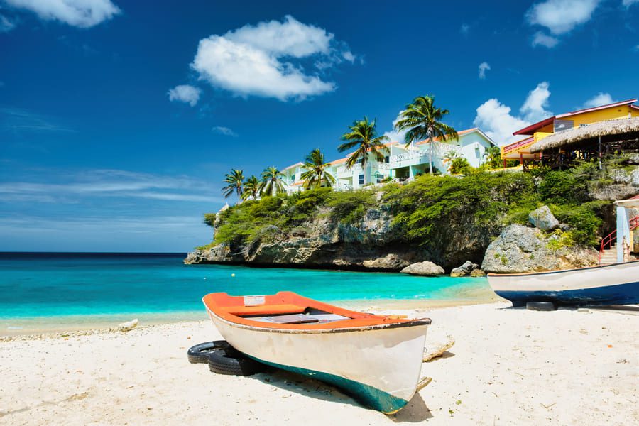 Colourful fishing boat on a pristine tropical beach with turquoise waters, palm trees, and luxury cliffside villas under a clear blue sky in Mexico.