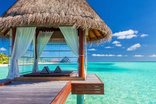 Luxury overwater spa pavilion in the Maldives, with white curtains, tropical ocean views, and clear turquoise water below.