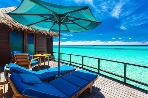 Private deck with sun loungers and umbrella overlooking crystal-clear turquoise waters at a luxury overwater villa in the Maldives.