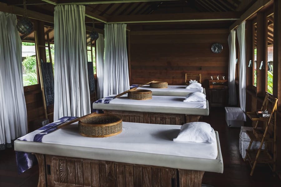 Luxury open-air spa treatment room with wooden massage tables and privacy curtains in a tropical setting