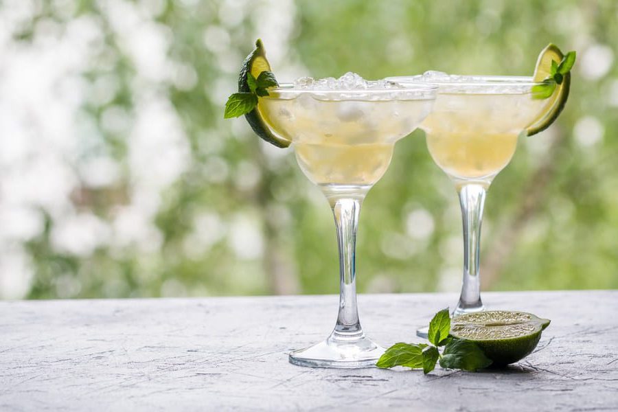 Two refreshing margarita cocktails garnished with lime and mint on a sunny outdoor table.