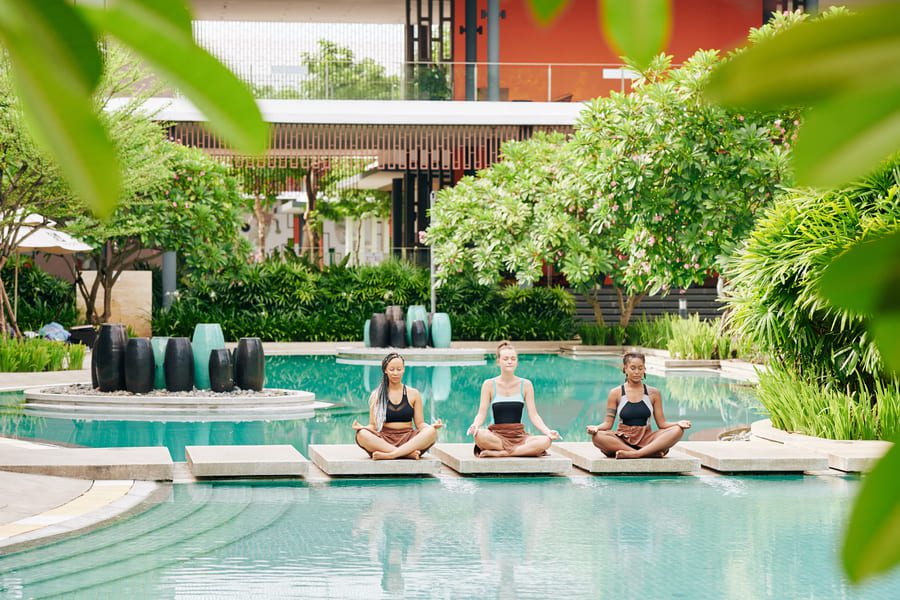 three women meditating outdoors in a serene Thai garden, experiencing a luxury wellness retreat in Thailand.