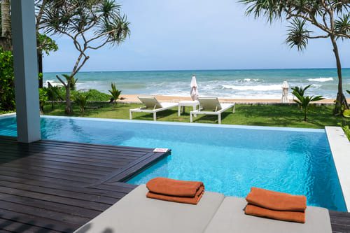 Private beachfront villa in Thailand featuring an infinity pool, sun loungers, and uninterrupted ocean views under a clear blue sky.