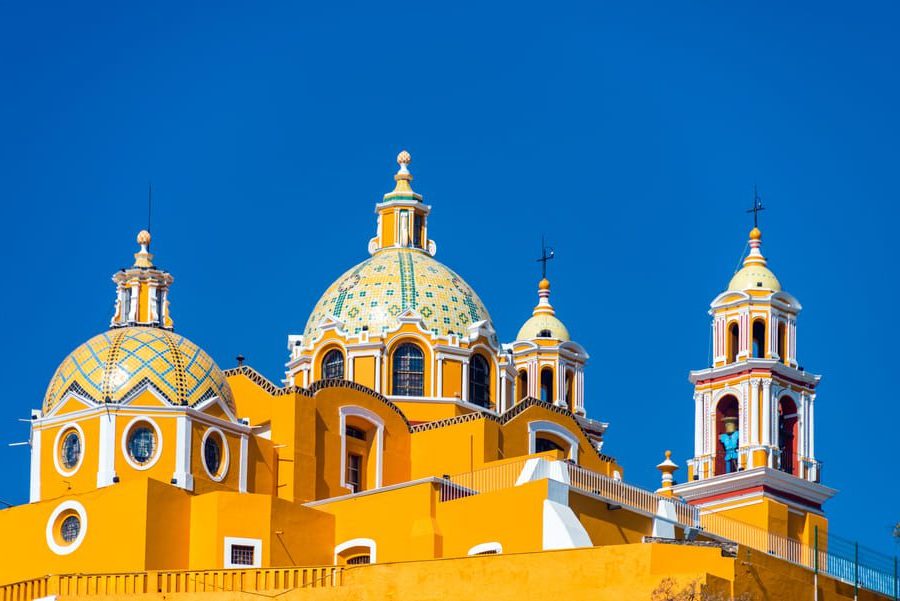 Colourful domes and towers of the Church of Our Lady of Remedies in Cholula, Mexico, set against a vibrant blue sky.