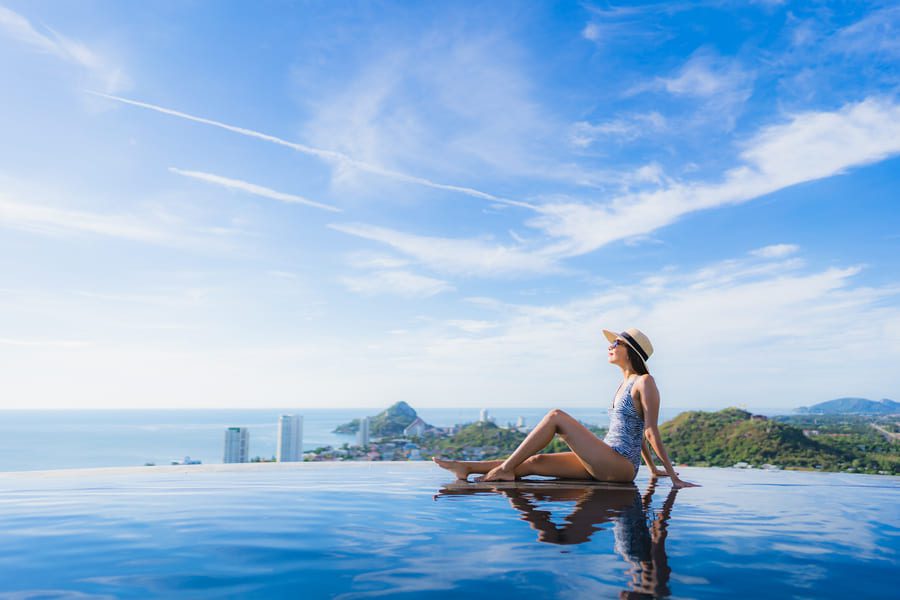 Smiling woman enjoying a luxury beachfront resort experience in Thailand, framed by tropical sunshine.